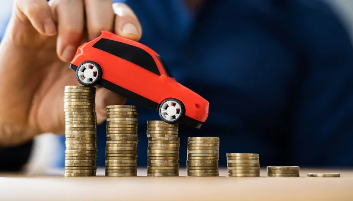 Dicas para economizar no Seguro Auto Manaus representado por um carrinho em cima de uma pilha de moedas.
