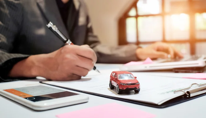 Vantagens de Contratar um Seguro auto Manaus representado por um homem escrevendo com um carrinho ao lado e uma calculadora.