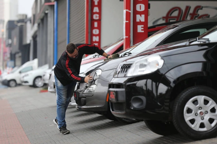 Homem organiza carros em uma loja de seminovos. Como consultar tabela FIPE pela placa?