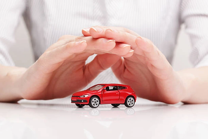 Pessoa com as mãos cobrindo uma miniatura de carro na cor vermelha. Falando sobre os melhores seguros para carros.