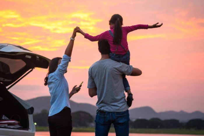 Família de pai, mãe e filha felizes, observando o entardecer em meio a viagem. Explicando o que é carta verde.