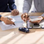 Corretor instrui cliente a assinar apólice de seguro. Há uma miniatura de carro sobre a mesa. Falando sobre os melhores seguros para carros.
