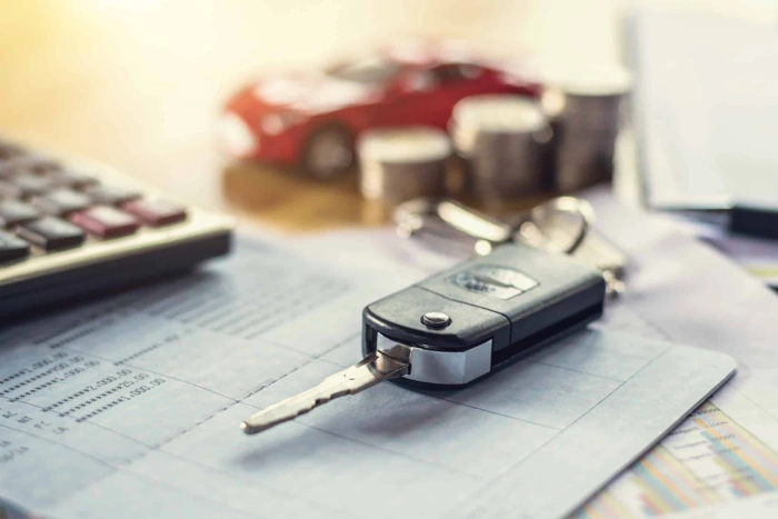 Estão sobre uma mesa: uma chave canivete, uma calculadora, um carro em miniatura na cor vermelha e alguns montinhos de moedas. Falando sobre os melhores seguros para carros.