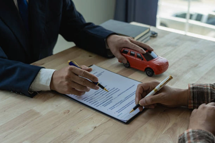 Corretor explica apólice de seguro a cliente, que já vai assiná-la. Há uma miniatura de carro vermelho sobre a mesa. Explicando qual o melhor seguro para carros e mais barato.