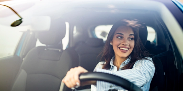 Mulher sorridente dirige o seu carro. Explicando qual o melhor seguro para carros e mais barato.