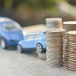 Duas miniaturas de carro na cor azul, um em frente ao outro, próximos a pilhas de moedas. Falando sobre o valor do seguro carros.
