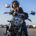 Mulher afivela o seu capacete para começar viagem com moto. Explicando a partir de quantas cilindradas precisa de habilitação.