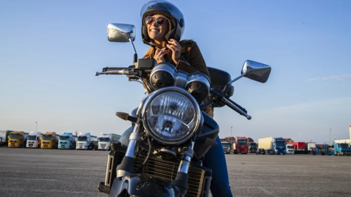 Mulher afivela o seu capacete para começar viagem com moto. Explicando a partir de quantas cilindradas precisa de habilitação.