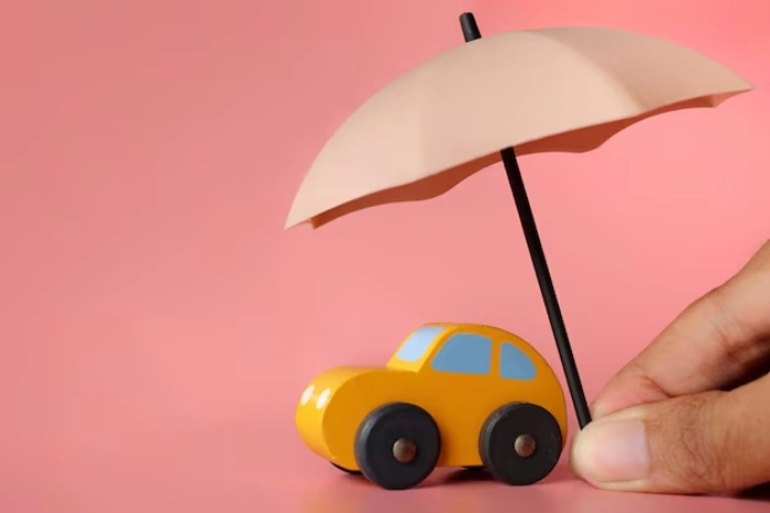 Pessoa segura mini guarda-chuvas sobre um carrinho de brinquedo em miniatura. Explicando qual a diferença entre seguro e proteção veicular.