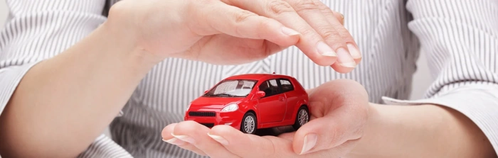 Pessoa segura carro em miniatura na cor vermelha. Falando sobre preço de seguro para carros.