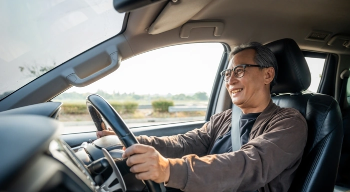 Idoso sorridente dirige seu veículo. Falando sobre seguro mais barato para carro.