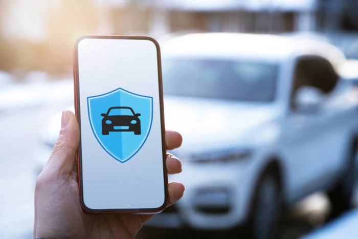 Pessoa segurando celular com símbolo que representa seguro de carro. Ao fundo, um veículo branco. Falando sobre o melhor seguro para carros antigos.