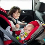 Duas crianças no banco de trás de um veículo. O menor está em um bebê conforto. Falando sobre qual é a cadeirinha certa para cada idade.