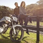 Casal posa para foto com Honda Fan 160 em um ambiente natural. Falando sobre o seguro fan 160.