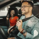 Motorista de app sorridente com sua passageira também alegre. Falando sobre seguro para carro de aplicativo.