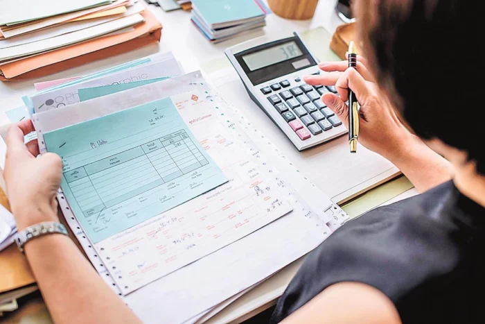 Mulher usa calculadora para fazer contas com vários documentos na mão. Explicando como declarar indenização de seguro de automóvel.