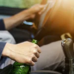 Homem dirigindo enquanto segura garrafa de bebida alcoólica. Explicando que embriaguez de motorista não isenta seguradora de pagar indenização.