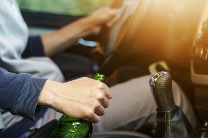 Homem dirigindo enquanto segura garrafa de bebida alcoólica. Explicando que embriaguez de motorista não isenta seguradora de pagar indenização.