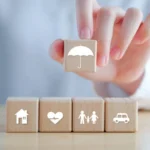 Pessoa posiciona blocos com símbolos que representam seguros. Falando sobre a melhor corretora de seguros.