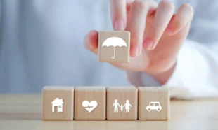 Pessoa posiciona blocos com símbolos que representam seguros. Falando sobre a melhor corretora de seguros.