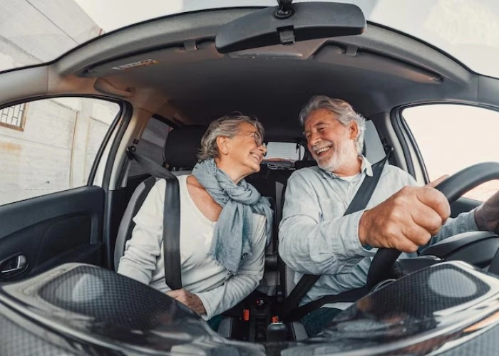 Casal de idoso felizes se olham e sorriem dentro de um carro. Falando sobre seguro de carro para idoso é mais barato.